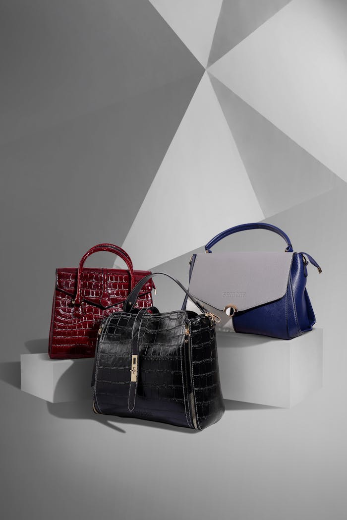 Stylish leather handbags displayed on a geometric studio background.